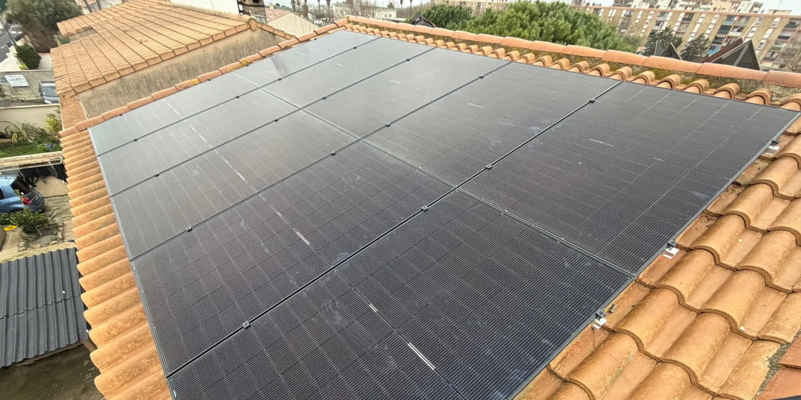 Vue rapprochée d'un champ de panneaux photovoltaïques noirs sur une toiture en tuiles, installation JM Consulting dans l'Hérault