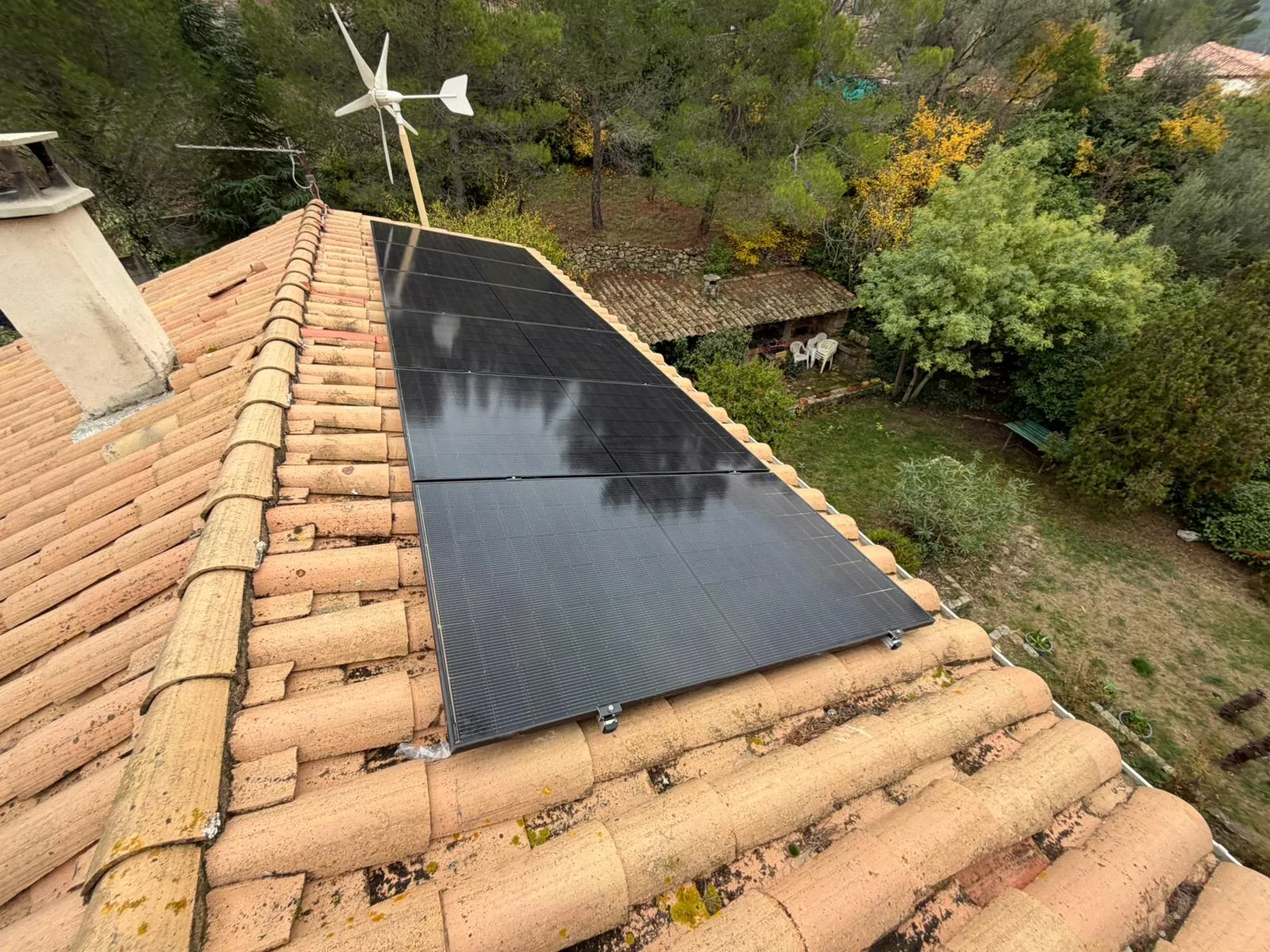 Panneaux photovoltaïques noirs posés sur une toiture en tuiles canal, au-dessus d'un jardin arboré, installation JM Consulting dans l'Hérault